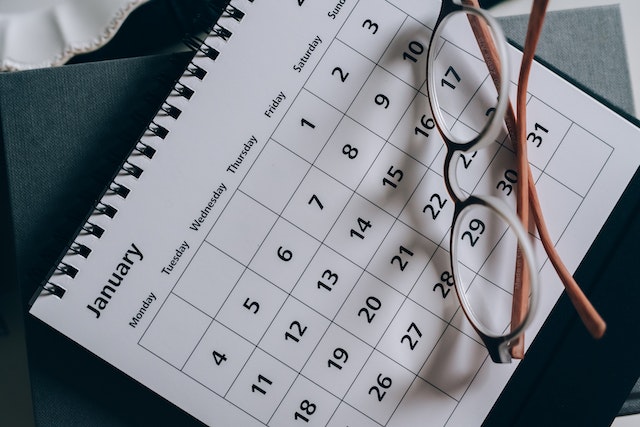 a pair of brown plastic reading glasses sit on top of a plain white desktop calendar with black text
